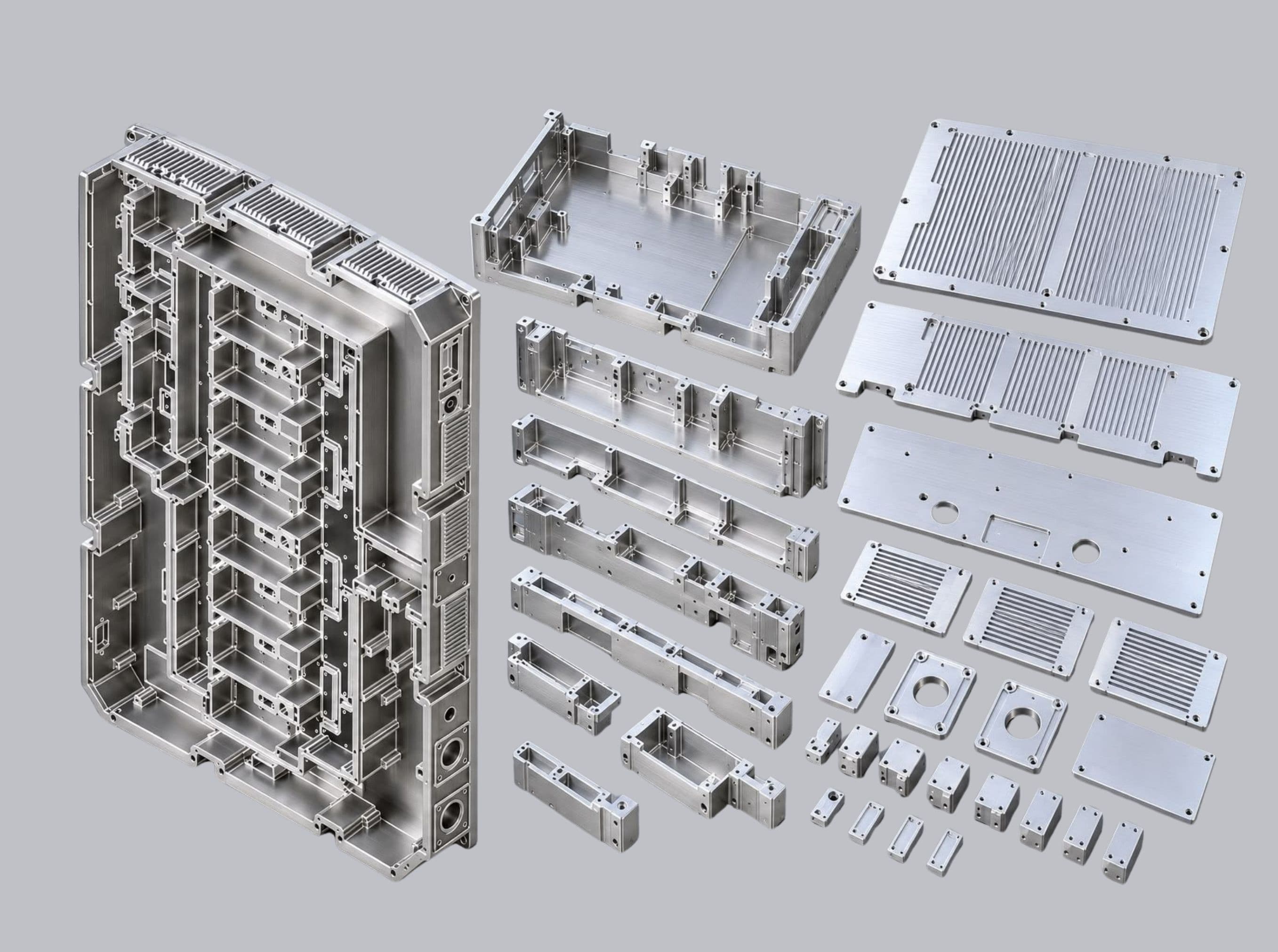 A tall machined housing with ribbed cooling fins beside a range of smaller milled brackets, frames, vented covers and blocks.