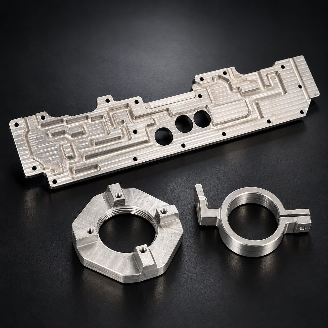 A long profiled plate with pockets and three bored holes, with an octagonal threaded ring and a threaded clamp ring in front of it.