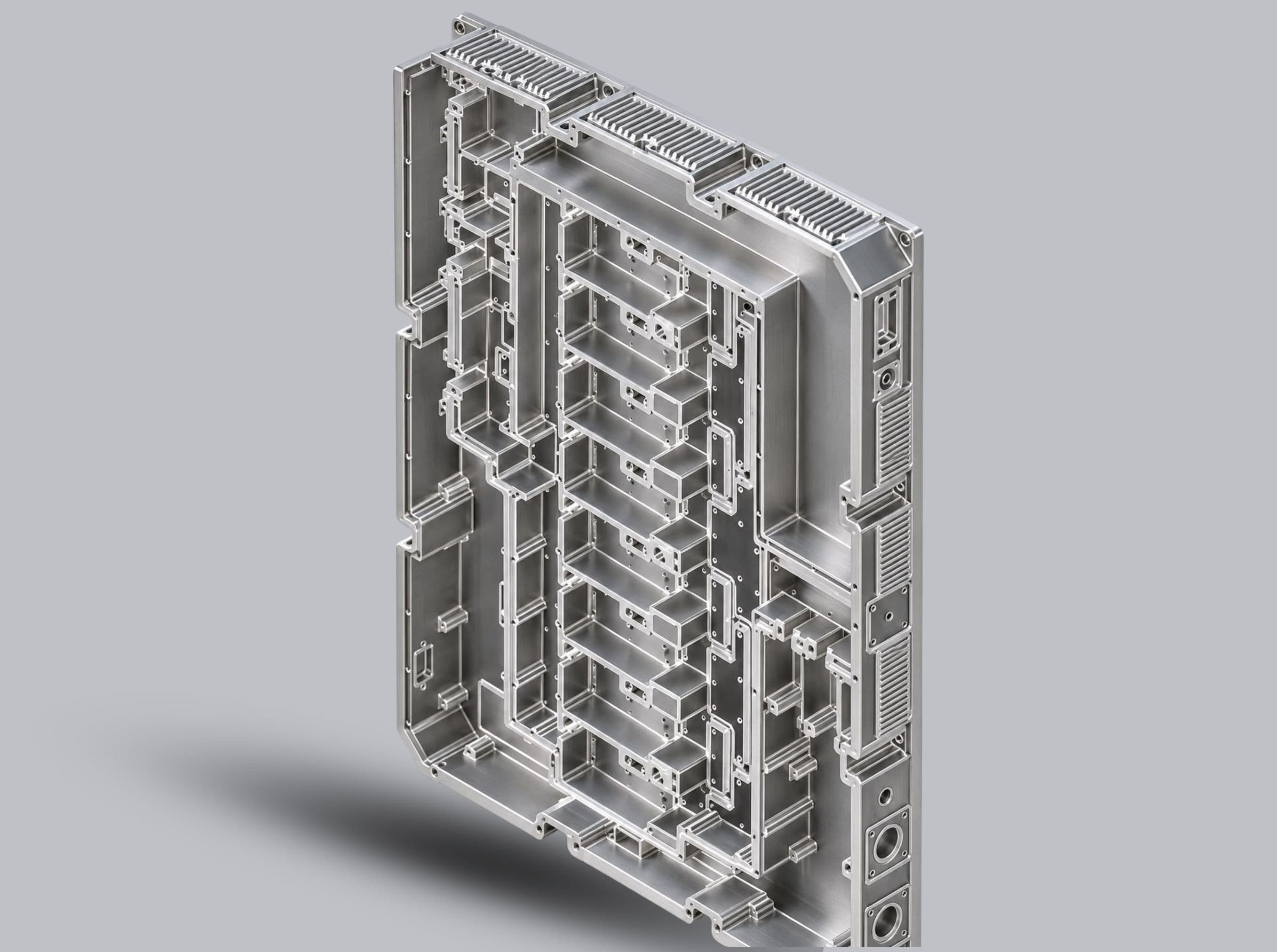 Upright machined housing with deep rectangular cavities, thin walls and finned sections along the top edge.
